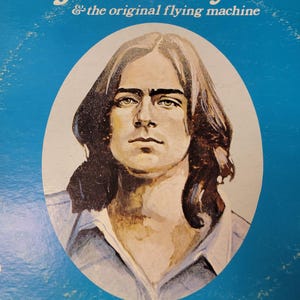 May include: Album cover for James Taylor & the original flying machine. The album art features a portrait of James Taylor in an oval frame against a blue background. The album title is in white script at the top.