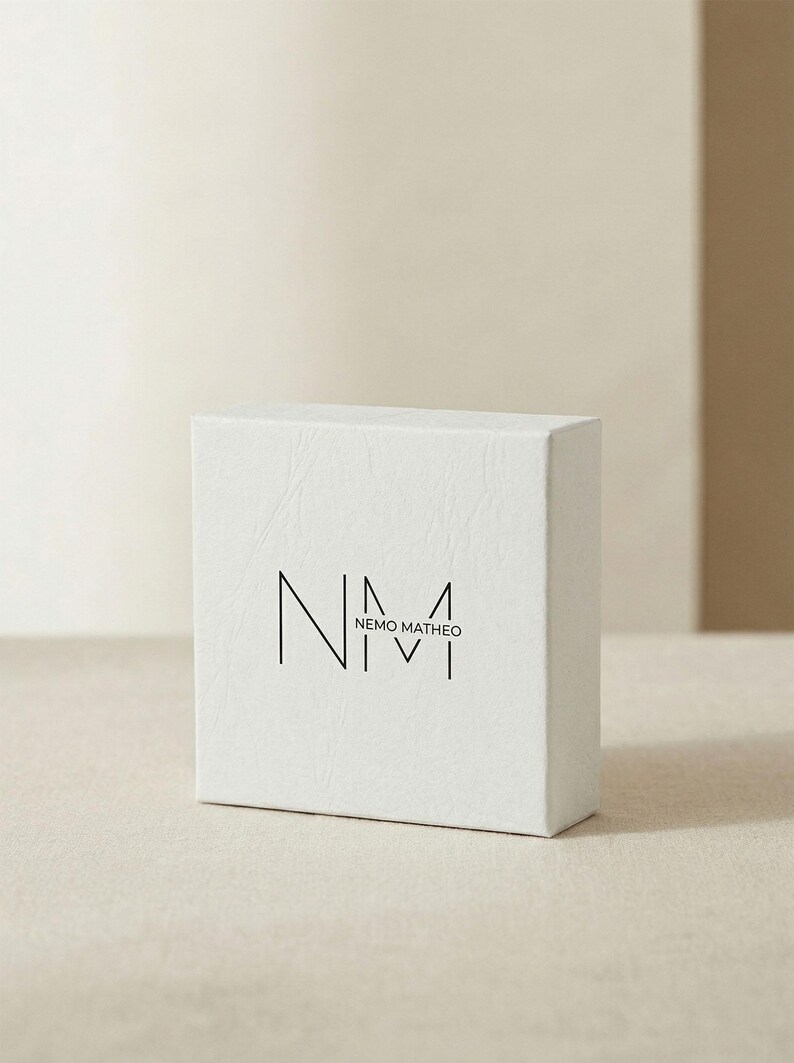 May include: A white, textured box with the logo "NEMO MATHEO" printed in black. The box is rectangular and sits on a neutral-toned surface. The logo features stylized letters and numbers.