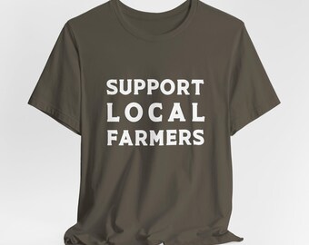 Może przedstawiać: Koszulka w ciemnobrązowym kolorze z nadrukiem "SUPPORT LOCAL FARMERS" w kolorze białym.