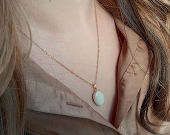 May include: A gold chain necklace with a white oval pendant. The pendant is smooth and has a subtle shine.
