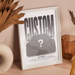 Puede incluir: Una impresi&oacute;n enmarcada en blanco con la palabra "CUSTOM" en texto negro y una silueta de un coche con un signo de interrogaci&oacute;n en el parabrisas. La impresi&oacute;n est&aacute; sobre una mesa con un jarr&oacute;n de hojas de palma secas y un jarr&oacute;n de vidrio marr&oacute;n.