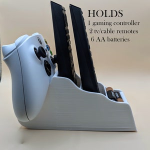 Puede incluir: Soporte de mando de juego de plástico blanco con ranuras para dos mandos a distancia y un compartimento para seis pilas AA.  HOLDS 1 gaming controller 2 tv/cable remotes 6 AA batteries