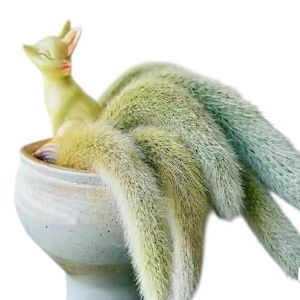 May include: A whimsical ceramic planter featuring a light green fox figurine resting inside. The planter is filled with a cascading, fuzzy, light green plant with hints of blue. The pot is a light blue-grey color.
