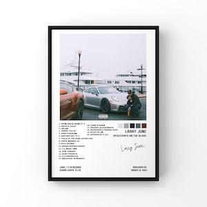 May include: A framed poster featuring the album art for "Spaceships on the Blade" by Larry June. The image shows a man near a silver car, with a marina in the background. The poster includes the album's tracklist, artist name, and release date.
