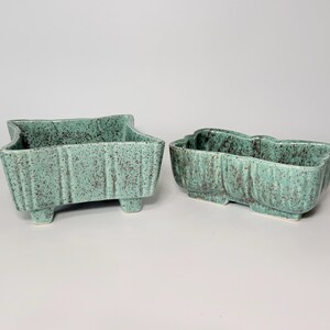 May include: Two vintage ceramic planters in a speckled turquoise glaze. One is rectangular with a scalloped top and three feet. The other is a long, curved planter with a similar speckled finish. Both are decorative.