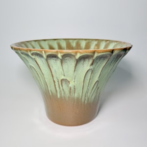 May include: A ceramic vase with a flared, scalloped rim. The vase features a two-tone glaze, with a light green color on the upper portion that drips down to a brown base. The vase has a wide opening and a smooth, glossy finish.
