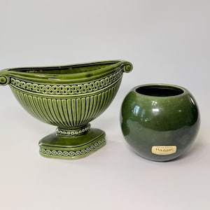 May include: Two green ceramic vases. One is a large, boat-shaped vase with a pedestal base and decorative trim. The other is a small, round vase with a glossy finish. The vases are a similar shade of green.