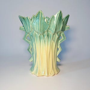 May include: A ceramic vase with a unique design. The vase features a light green and yellow color scheme. The top of the vase has a leaf-like design, and the sides have a zig-zag pattern. The vase is approximately 10 inches tall.