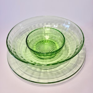 May include: A collection of vintage green glass bowls and plates. The set includes a small, medium, and large bowl, along with a large plate. The bowls have a ribbed design, and the plate has a smooth surface. The glass is a light green colour.