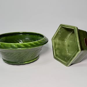 May include: Two green ceramic planters. One is a round, low bowl with a decorative leaf pattern around the base. The other is a hexagonal planter with a small, rectangular label on the side. Both have a glossy finish.