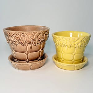 May include: Two ceramic plant pots with matching saucers, one in a light brown and one in a bright yellow. Each pot features a raised, textured leaf pattern around the upper rim and a grid-like, embossed square design on the main body.