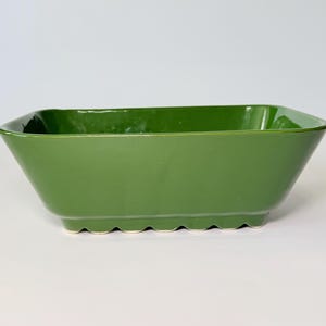 May include: A rectangular, green ceramic planter with a glossy finish. The planter has a slightly trapezoidal shape with a scalloped base. The interior is also green.