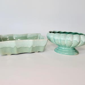 May include: Two ceramic planters in a light green color. One is rectangular with a wavy edge, and the other is a pedestal bowl with a scalloped rim. Both have a glossy finish and are set against a white background.