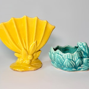May include: Two ceramic vases. One is a bright yellow fan-shaped vase with a textured surface. The other is a turquoise frog-shaped planter with a wavy rim and leaf details. Both are on a light gray background.