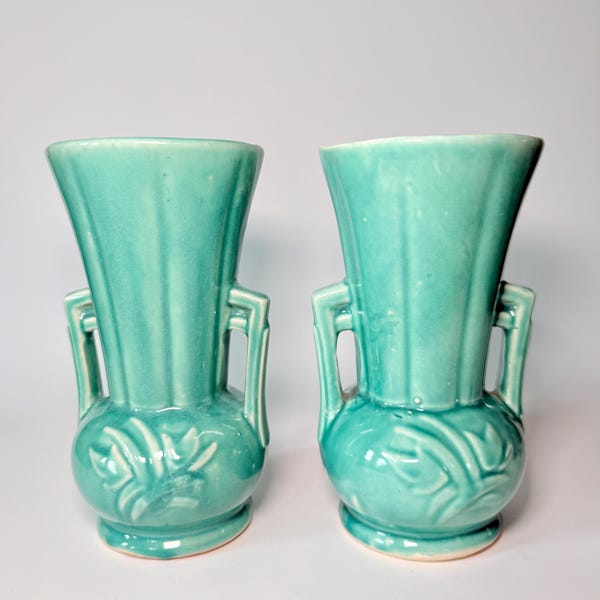 Peut inclure: Deux vases assortis en céramique turquoise. Chaque vase a un dessus évasé, deux anses et un motif floral décoratif sur la base bulbeuse. Les vases sont présentés sur fond blanc.