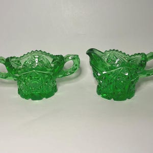 May include: A pair of vintage green glass serving dishes. One is a sugar bowl with two handles, and the other is a creamer with a spout and a handle. Both have a detailed, textured pattern.