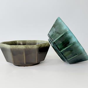 May include: Two ceramic bowls with a geometric design. One bowl is dark brown with a green rim, and the other is teal with a glossy finish. The bowls have a faceted, octagonal shape and are set against a white background.