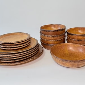 Peut inclure: Un ensemble de vaisselle en céramique marron, comprenant des assiettes et des bols. Les assiettes sont empilées, avec une grande assiette en bas. Les bols sont en deux piles et un seul bol. Les bords ont une bordure marron plus foncée.