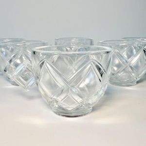 May include: A set of clear glass teacups with diamond-shaped cut glass patterns. Each cup has a small handle and a rounded bowl shape. The cups are arranged on a white surface.
