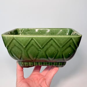 May include: A square, deep green ceramic bowl featuring a raised diamond pattern along the exterior sides and a decorative beaded texture around the base. The bowl has a glossy finish and a wide, open top with a smooth, uniform rim.
