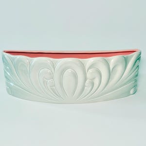May include: A decorative, oval-shaped planter with a light blue exterior and a pink interior. The planter features a repeating, stylized leaf design. The planter is approximately 12 inches long.