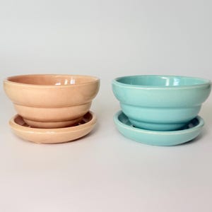 May include: Two ceramic plant pots, one peach and one turquoise, each with a matching saucer. The pots have a tiered design and a glossy finish. Ideal for small plants or succulents.