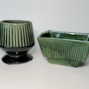 May include: A round, ribbed green ceramic planter with a dark base sits beside a rectangular, ribbed green ceramic planter. Both vessels feature a glossy finish and vertical textured lines, showcasing a consistent color palette and design style.