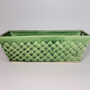 May include: A rectangular, green ceramic planter with a diamond pattern. The planter has a slightly textured surface and a light green colour. The planter is designed for indoor or outdoor use.