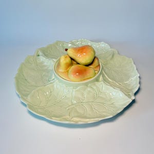 May include: A light green ceramic serving dish with a leaf design. The dish has a central bowl filled with ceramic pears. The pears are yellow and red. The dish is round with four sections.