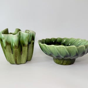 May include: Two ceramic decorative pieces. One is a tall, ruffled vase with a green and brown glaze. The other is a low, pedestal bowl with a leaf-like design and a green glaze. Both pieces have a glossy finish.