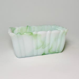 May include: A rectangular glass dish with a ruffled edge. The dish is white with green marbling. The sides have a vertical ribbed pattern. The dish is empty and sits on a white surface.