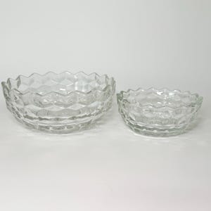 May include: Two clear glass bowls with a textured, geometric design. The larger bowl is on the left, and the smaller bowl is on the right. Both bowls have a wavy, scalloped rim.