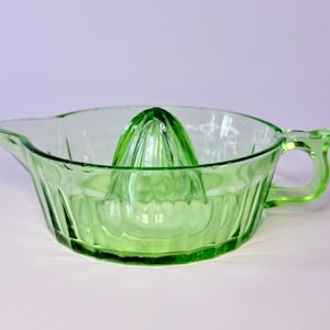 May include: A vintage green glass citrus juicer with a built-in reamer and a pouring spout. The juicer has a handle and a ribbed design on the bowl. This kitchenware item is perfect for making fresh juice.