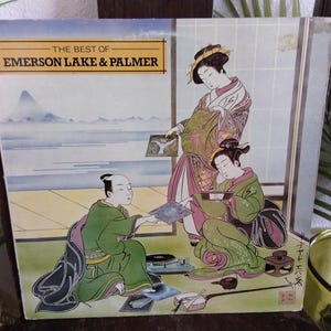 May include: Vintage vinyl record album cover for "The Best of Emerson, Lake & Palmer." The cover art features a Japanese-style illustration of three figures in traditional clothing, with a landscape in the background. The album cover is in good condition.