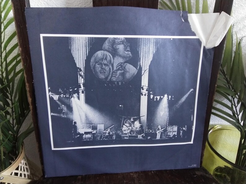 May include: A black and white concert poster featuring a band performing on stage. The poster has a dark blue background with a white border. The band members' faces are visible at the top, and the stage is lit with spotlights.