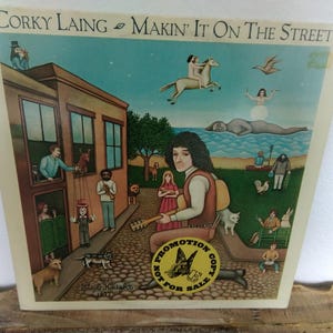 May include: Vintage album cover art for Corky Laing's "Makin' It On The Street." The illustration depicts a street scene with figures, animals, and a musician. The cover has a "Promotion Copy Not For Sale" sticker.