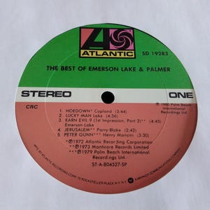 May include: A vinyl record for "The Best of Emerson Lake & Palmer" album. The record label is green and salmon-colored, with the Atlantic Records logo. The tracklist includes "Hoedown," "Lucky Man," and "Karn Evil 9."