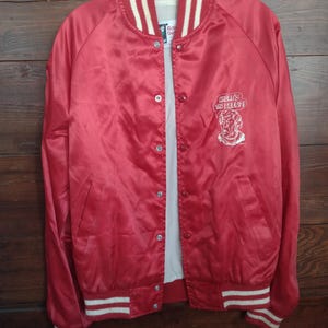 May include: A red satin bomber jacket with white and cream striped accents on the collar, cuffs, and hem. The jacket features a button-up front and a white graphic on the chest that says "Where's the Beef?"
