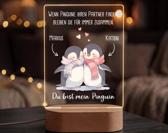 May include: A rectangular acrylic night light with a wooden base featuring two illustrated penguins wearing scarves, three small pink hearts, and German text that reads: Wenn Pinguine ihren Partner finden, bleiben sie für immer zusammen. Markus, Katrin, Du bist mein Pinguin.