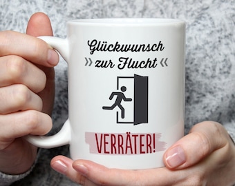 May include: White ceramic mug with a handle, featuring the German text "Glückwunsch zur Flucht" above a graphic of a person running through a door. Below is the word "VERRÄTER!" in a red banner.