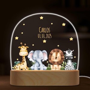 Könnte beinhalten: Eine Holz-Nachtlampe mit einer klaren Acrylglocke, die eine Giraffe, einen Elefanten, einen Löwen und ein Zebra zeigt. Die Glocke wird mit einem warmweißen Licht beleuchtet. Der Text "CARLOS 01.01.2025" ist auf die Glocke gedruckt.