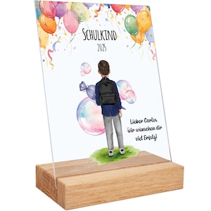 Puede incluir: Un letrero decorativo con base de madera presenta una ilustración en acuarela de un niño con mochila, rodeado de globos y burbujas. El texto "SCHULKIND 2025" se muestra en la parte superior. El letrero está diseñado para colocarse de pie.