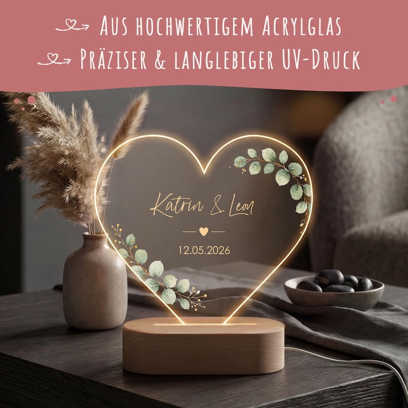 May include: A heart-shaped acrylic light with a wooden base, featuring the printed names Katrin & Leon, the date 12.05.2026, and green leaf illustrations. The top text reads: AUS HOCHWERTIGEM ACRYLGLAS and PR&Auml;ZISER & LANGLEBIGER UV-DRUCK.