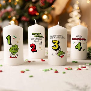 Könnte beinhalten: Vier weiße Säulenkerzen mit Grinch-Motiven. Jede Kerze zeigt eine Zahl von 1 bis 4, zusammen mit Grinch-Illustrationen und festlichem Text. Die Kerzen sind mit grünen, roten und gelben Akzenten verziert.