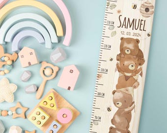 May include: A wooden growth chart with a light wood grain background features a series of brown bear illustrations. The chart includes the name "Samuel" and the date "12. 03. 2024". The chart measures up to 140 cm, with other wooden toys in the background.