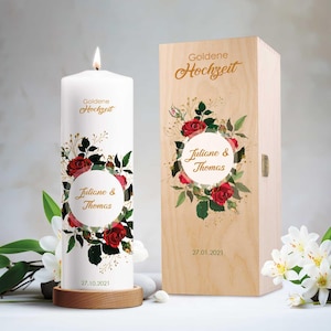 Könnte beinhalten: Eine weiße Kerze mit goldener Aufschrift "Goldene Hochzeit" und einem Blumendesign mit roten Rosen und goldenen Akzenten. Die Kerze befindet sich in einer Holzkiste mit der gleichen Aufschrift und dem gleichen Blumendesign. Die Kiste enthält auch die Namen "Juliane & Thomas" und das Datum "27.01.2021".