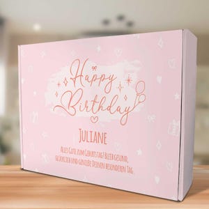 Op de afbeelding: Roze cadeaudoos met een wit en roze ontwerp. De doos heeft een happy birthday-boodschap met de naam Juliane en de tekst "Alles Gute zum Geburtstag! Bleib gesund, glücklich und genieße deinen besonderen Tag."
