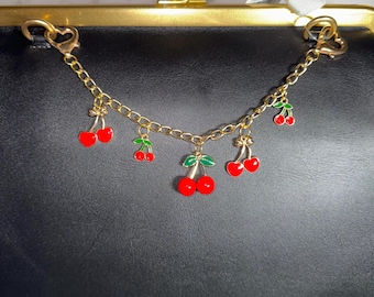 May include: A black leather purse with a gold clasp and a gold chain with cherry charms.