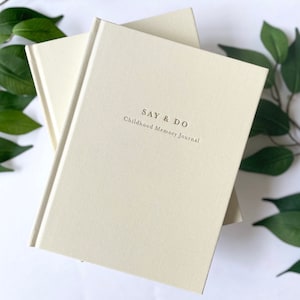 May include: Two cream-colored journals with a gold embossed title, "SAY & DO Childhood Memory Journal".