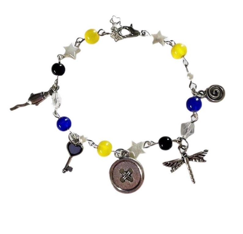 May include: A silver-toned bracelet featuring yellow, blue, and black beads, along with star-shaped charms and decorative pendants. The bracelet includes a key, button, dragonfly, and other charms.